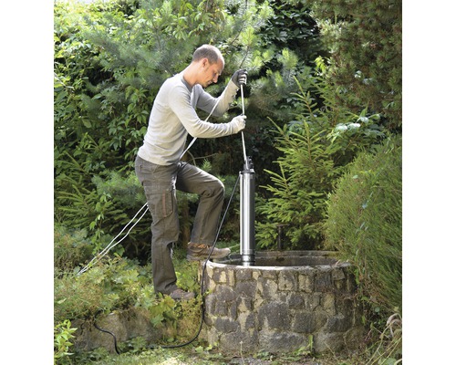 Muž instaluje hlubinné čerpadlo do studny na zahradě.