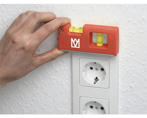 Ruka drží vodováhu na elektrické zásuvce, aby zkontrolovala vyrovnání.