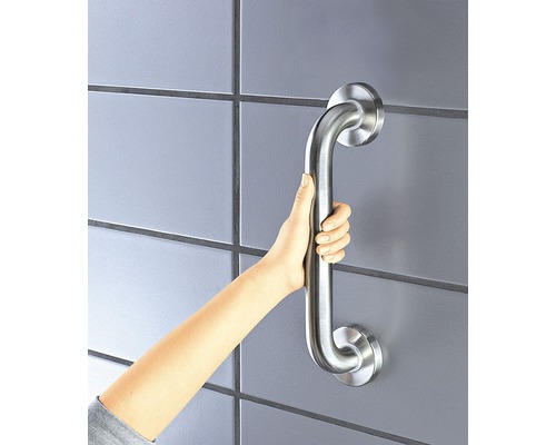 Ruka drží madlo na obložené zdi pro větší bezpečnost v koupelně.