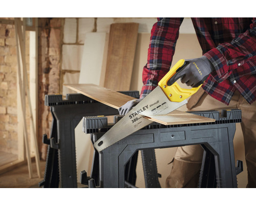 Osoba řeže kus dřeva na dvou kozech ruční pilou Stanley.