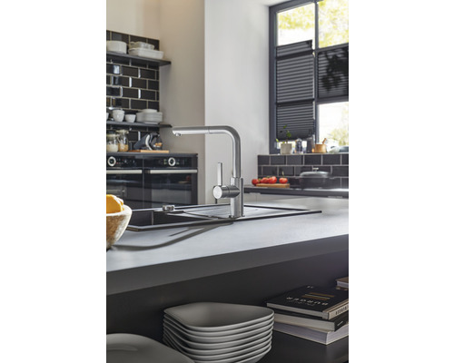 Kuchyňská scéna s dřezovou baterií, dřezem a kuchyňským náčiním na pracovní desce.