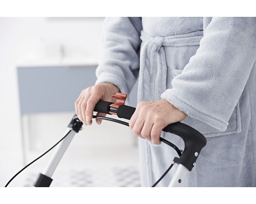 Detailní záběr osoby v županu používající chodítko.