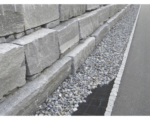 Opěrná zeď z šedých žulových bloků s štěrkovým ložem.