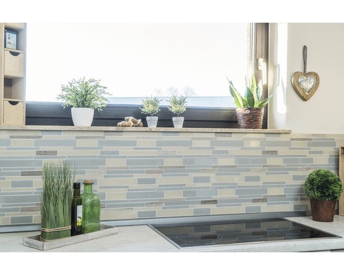 Kuchyňská scéna s obkladovou mozaikou na zdi, okenní parapet s dekorací a varná deska na pracovní desce.