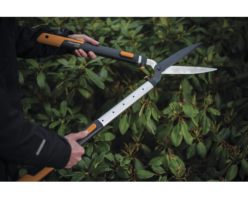 Osoba používá pákové nůžky na živý plot před zeleným živým plotem.