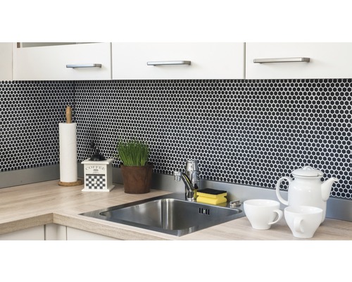 Kuchyňská scéna s dřezem, vodovodní baterií, mozaikovými obklady a kuchyňskými potřebami na pracovní desce.