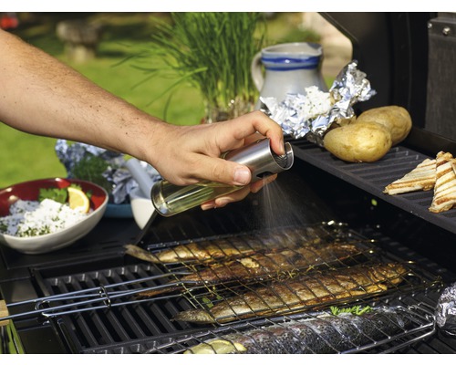 Osoba stříká olej na rybu na grilu.