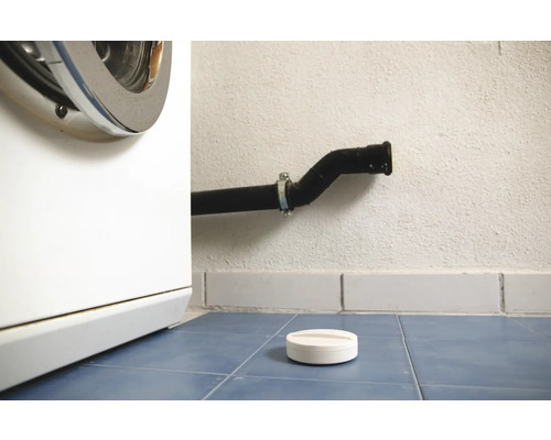 Pračka, odpadní trubka a dávkovací pomůcka na prací prostředek na modré dlažbě