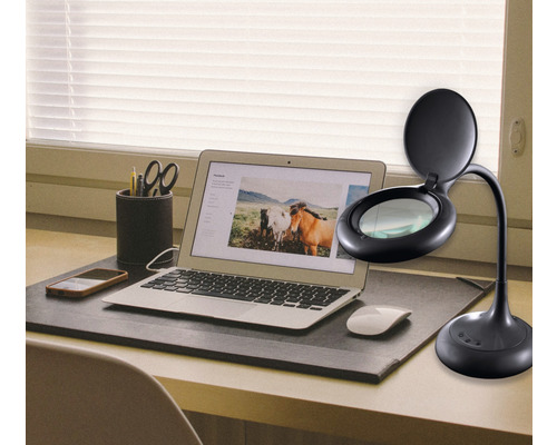 Stůl s notebookem, mobilním telefonem, stolní lampou s lupou a kancelářskými potřebami