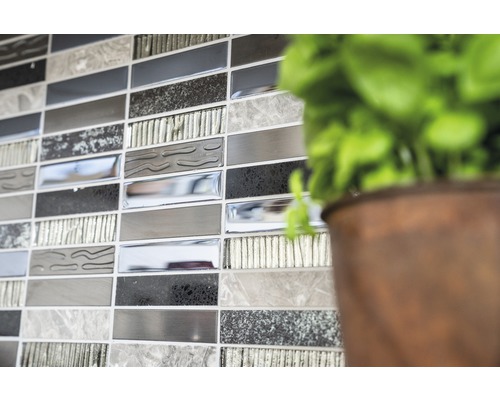 Detailní záběr stěny s mozaikovými obklady v různých odstínech šedé, vedle rostliny