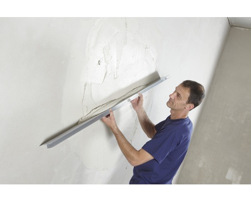 Muž vyrovnává stěnu pomocí omítkové latě