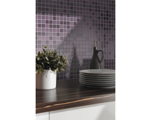 Kuchyňská scéna s mozaikovými obklady, pracovní deskou, nádobím, rostlinou a lahví na olej