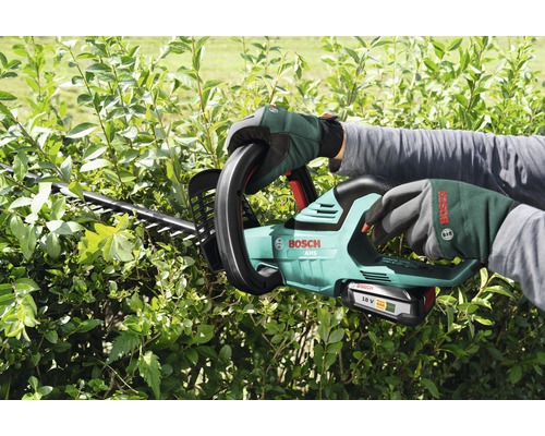 Osoba stříhá živý plot pomocí akumulátorových nůžek na živý plot Bosch
