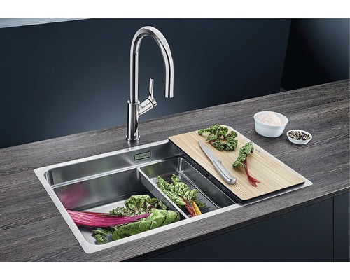 Dřez s baterií, krájecí deskou, mísou na zeleninu a nakrájenou zeleninou.