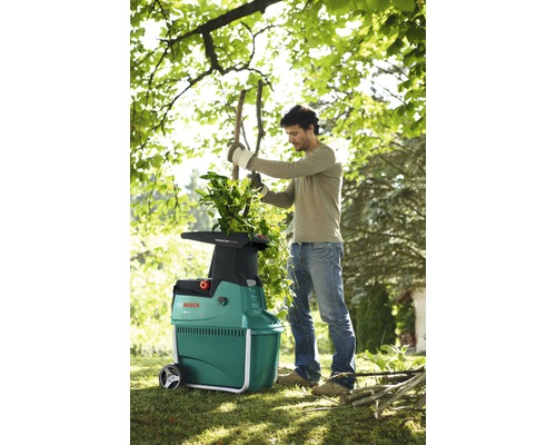 Muž používá zahradní drtič značky Bosch na zahradě.