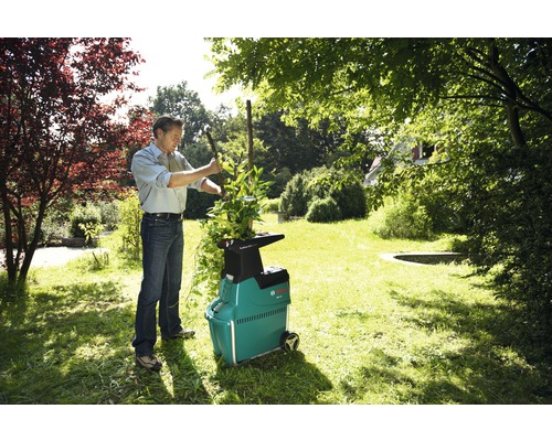 Muž plní zahradní drtič na zahradě větvemi.