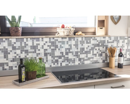 Kuchyňská scéna s mozaikovými obklady na zdi a varnou deskou na pracovní desce.