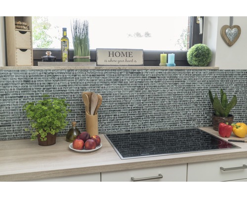 Kuchyňská scéna s mozaikovou stěnou, varnou deskou a kuchyňským náčiním na pracovní desce.