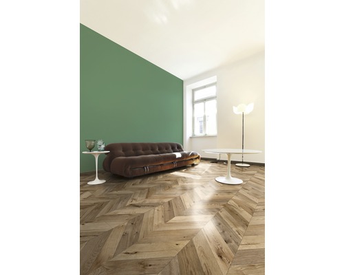 Obývací pokoj s hnědou pohovkou, dřevěnou podlahou se vzorem rybí kosti a zelenou stěnou