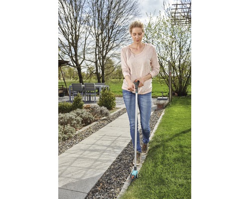 Žena používá v zahradě řezačku okrajů trávníku ke stříhání okrajů trávníku.