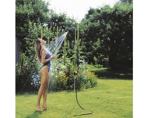 Žena pod zahradní sprchou na zahradě.