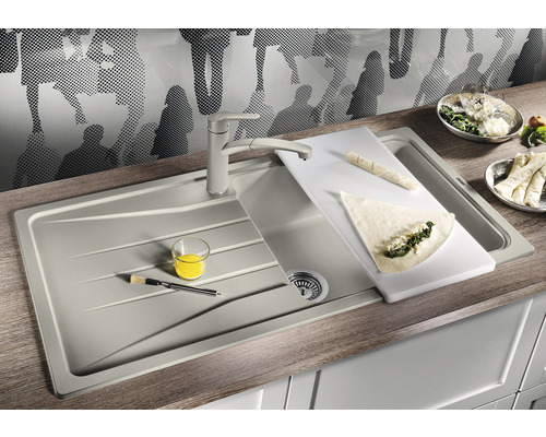 Dřez s krájecí deskou, kuchyňská baterie a jídlo na pracovní desce