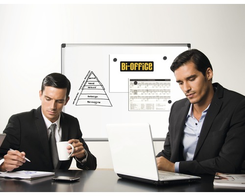 Dva muži sedí u stolu s notebookem před prezentací na tabuli v kanceláři.