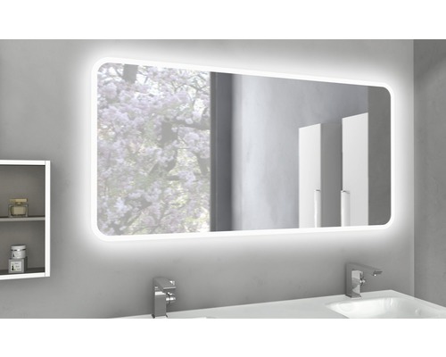 Osvětlené koupelnové zrcadlo nad umyvadlem s armaturami a malou poličkou.