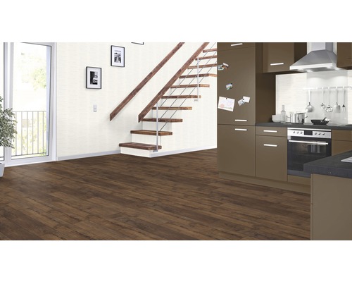 Interiér s hnědou laminátovou podlahou, schodištěm, kuchyní a balkonem.