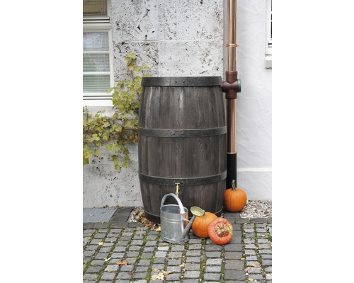 Dřevěný dešťový sud s kohoutkem, kovová konev a dýně na zahradě.