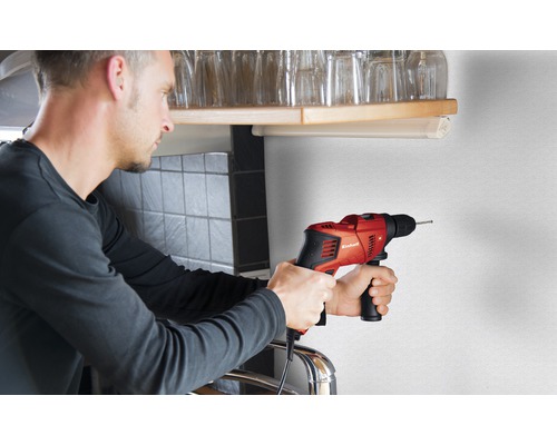 Muž vrtá díru do zdi červenou příklepovou vrtačkou Einhell