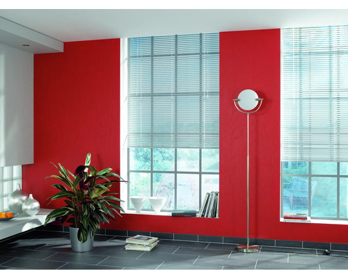 Světlá místnost se dvěma okny vybavenými žaluziemi, červenou stěnou a stojací lampou