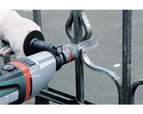 Osoba čistí železný plot drátěným kartáčem na vrtačce.