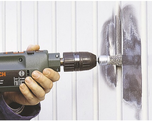 Osoba používá vrtačku s drátěným kartáčem na kovovém povrchu.