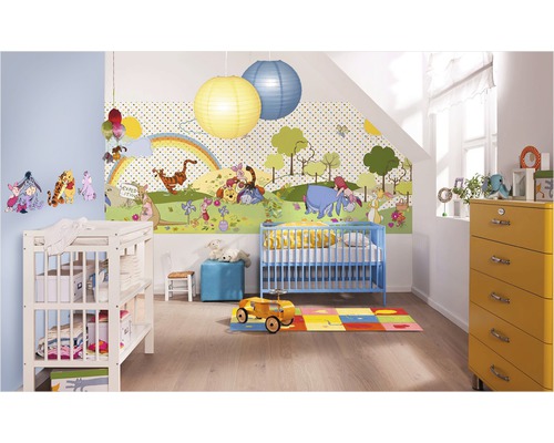 Dětský pokoj s tapetou Medvídek Pú, modrou dětskou postýlkou, přebalovacím pultem a žlutou komodou.