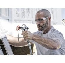 Muž používá stříkací pistoli k malířským pracím venku.