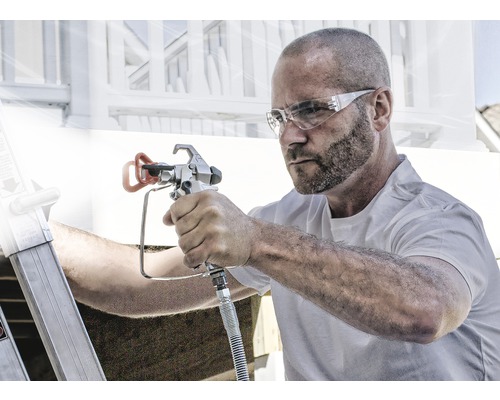 Muž používá stříkací pistoli k malířským pracím venku.