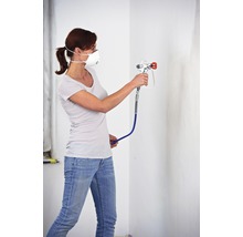 Žena s respirátorem a stříkací pistolí maluje stěnu