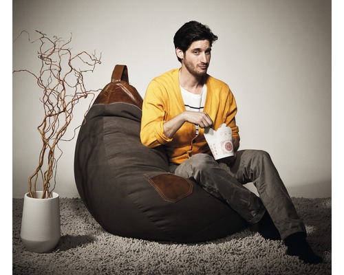 Muž sedí na hnědém sedacím vaku s koženými detaily a jí z krabičky s sebou