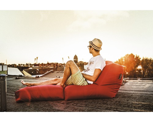 Muž s kloboukem relaxuje na červeném sedacím vaku s podnožkou na střeše