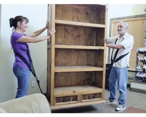 Dvě osoby přepravují dřevěnou knihovnu pomocí popruhů.