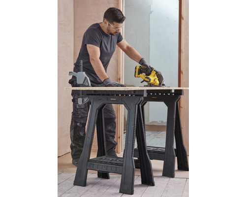 Řemeslník řeže dřevěnou desku na dvou kozách Stanley ve hrubé stavbě.