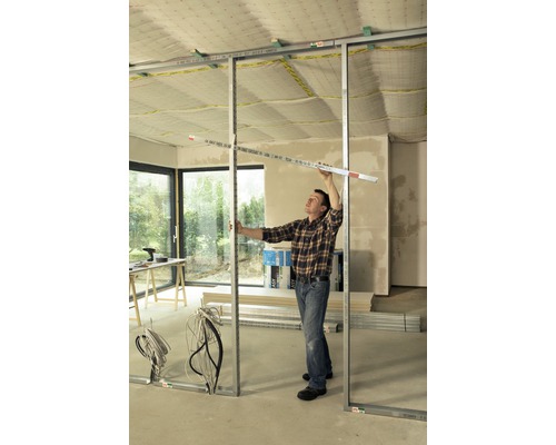 Muž montuje kovovou rámovou konstrukci s měřicím nástrojem v místnosti.