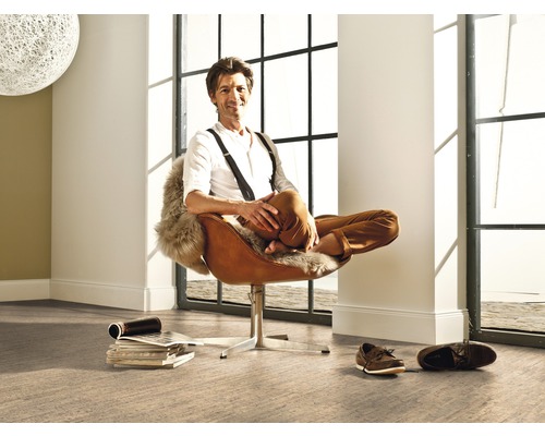 Muž sedí uvolněně v křesle ve světlé místnosti s velkým oknem a podlahovou krytinou.