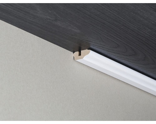 Dřevěná podlahová lišta připevněná ke zdi a tmavé dřevěné podlaze