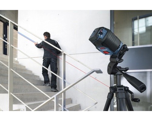 Staveniště s čárovým laserem na stativu a řemeslníkem na schodech