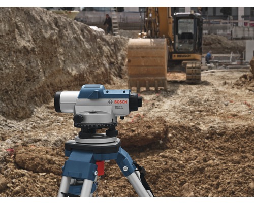 Stavební scéna s nivelačním přístrojem na stativu a bagrem v pozadí