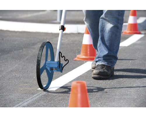 Osoba měří měřicím kolečkem na asfaltu