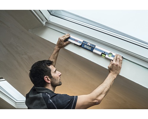 Řemeslník používá digitální vodováhu na rámu střešního okna.