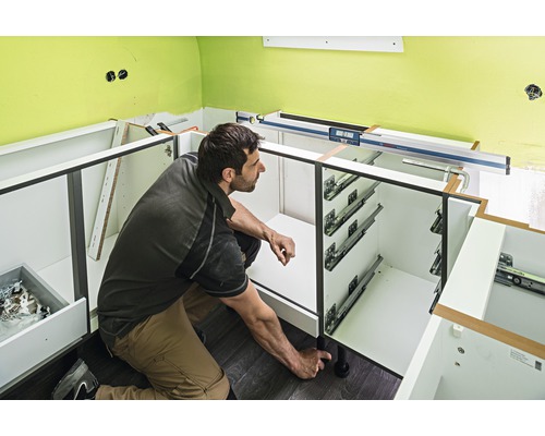 Muž montuje spodní kuchyňské skříňky s výsuvy a vyrovnávacími nožičkami.